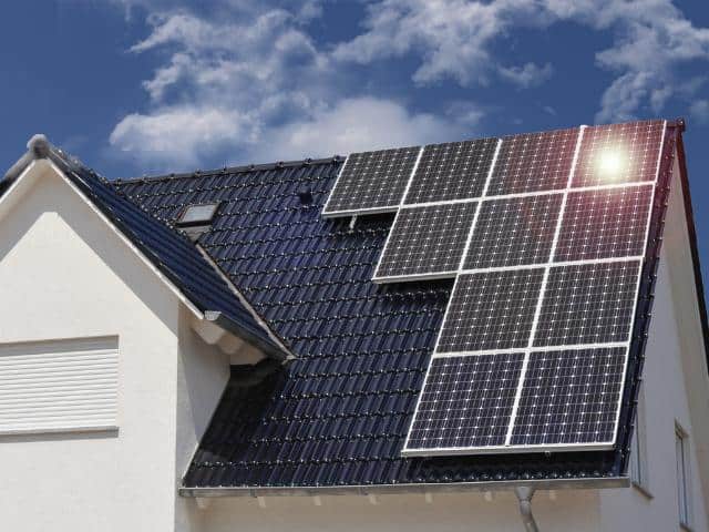 11 grote zonnepanelen op een dak van een wit huis.