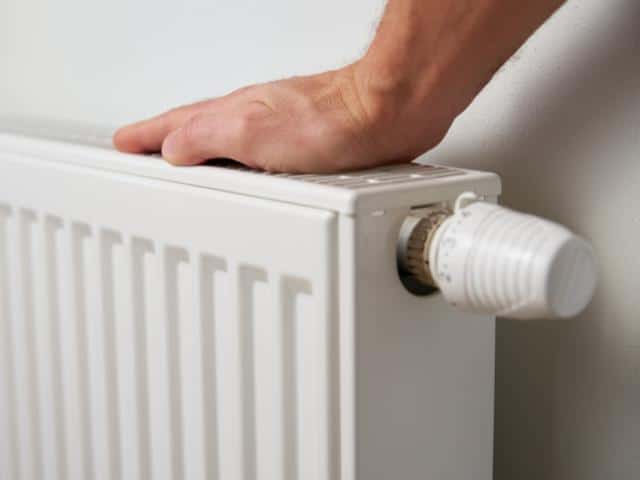 Hand controleert warmte van radiator met thermostaatknop.