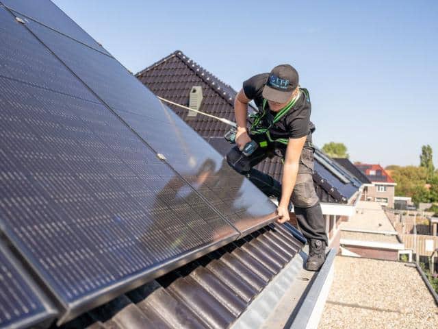 Technicus installeert zonnepanelen op een woonhuisdak